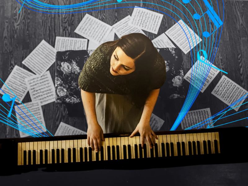 A birds eye view of Magdalene Taylor playing piano surrounded by sheet music on the ground around her.